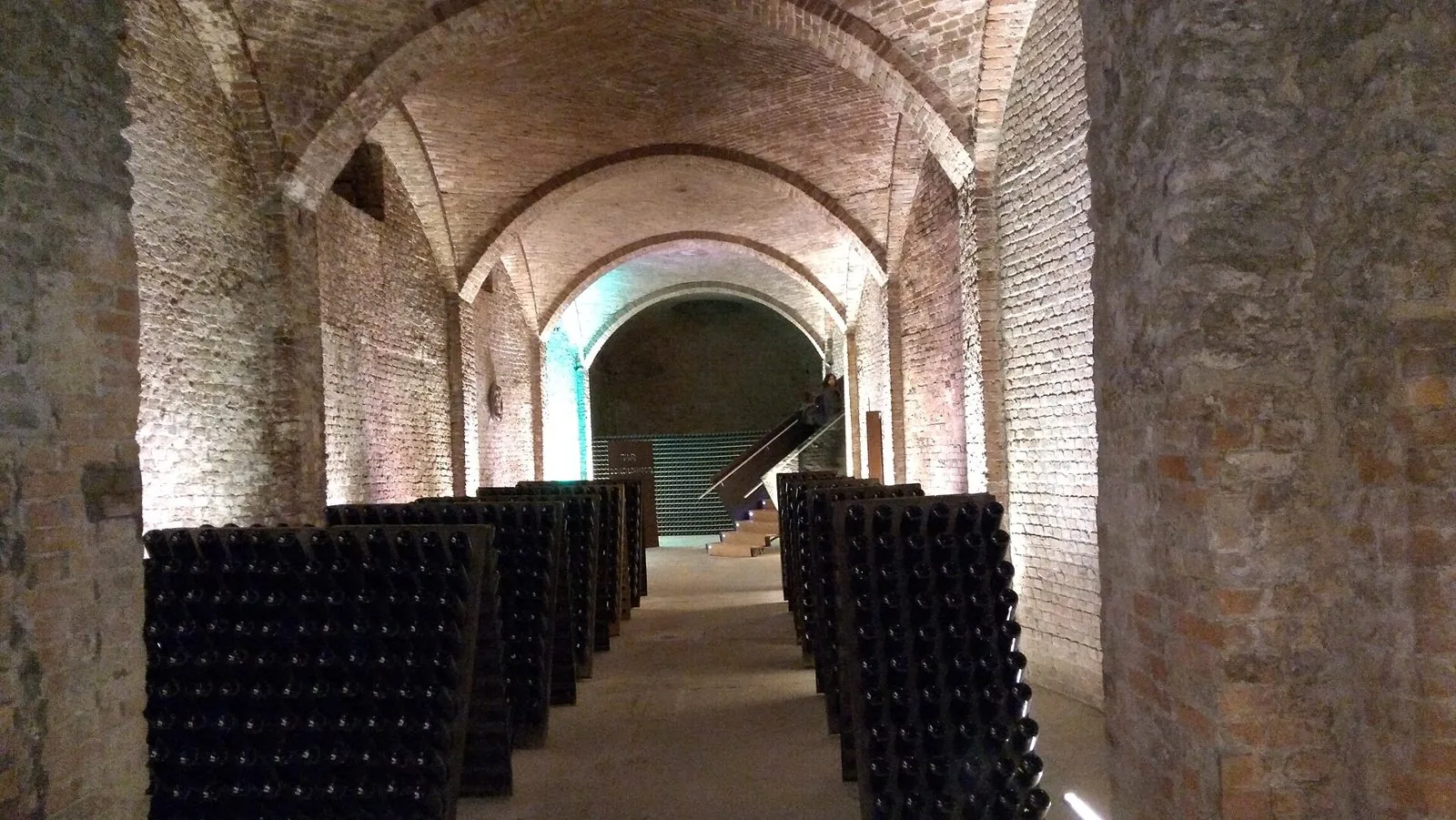 Una galleria sotterranea di Canelli con volte in mattoni a crociera e file di pupitre cariche di bottiglie di spumante