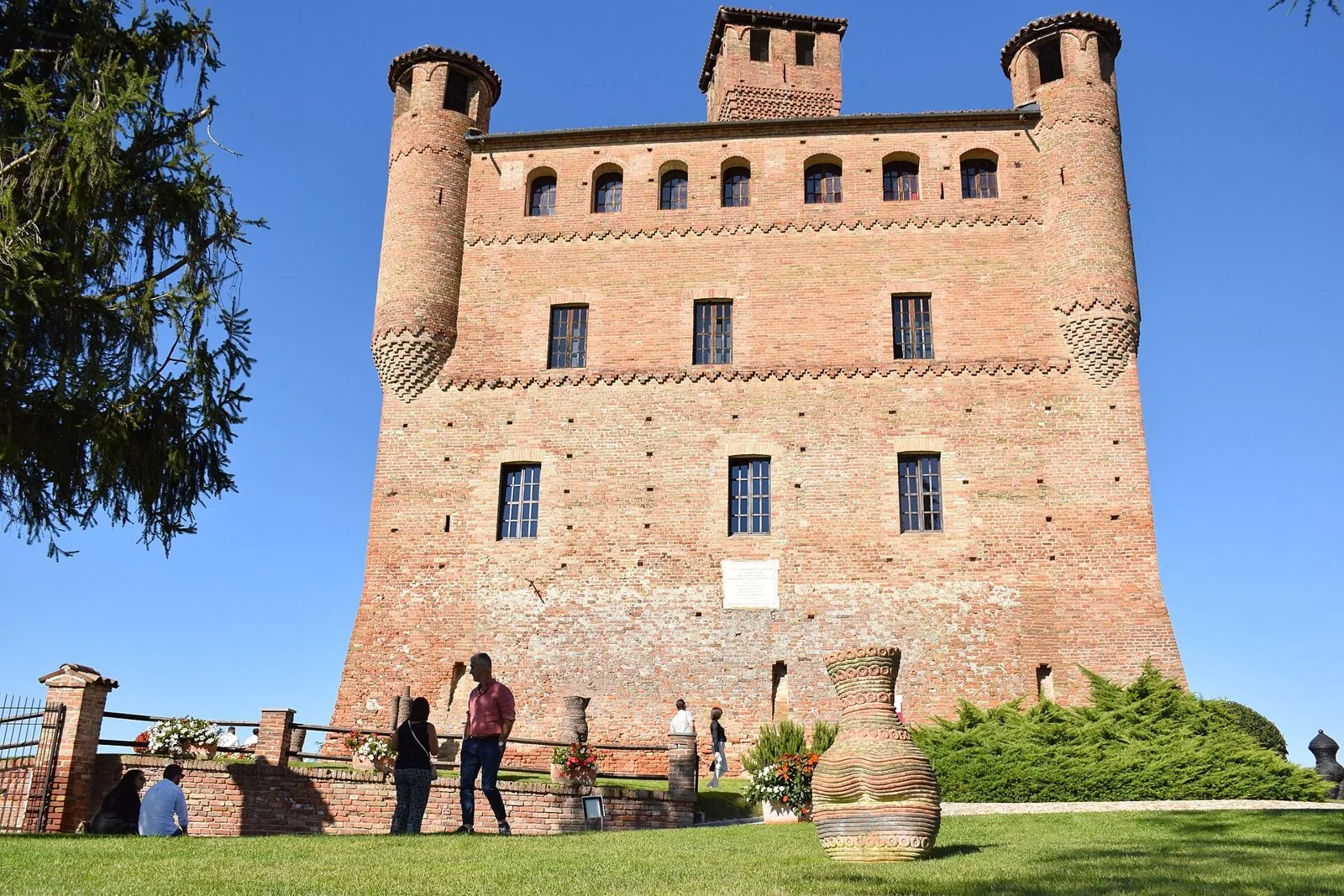 Il castello di Grinzane Cavour in mattoni rossi con torri angolari, sede dell'Enoteca Regionale Piemontese Cavour, sotto un cielo azzurro