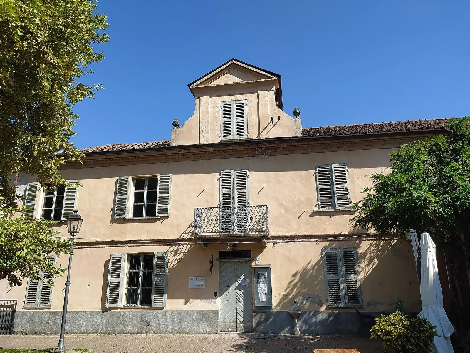 Facciata della casa natale di Cesare Pavese a Santo Stefano Belbo, con persiane verdi e piccolo balcone in ferro